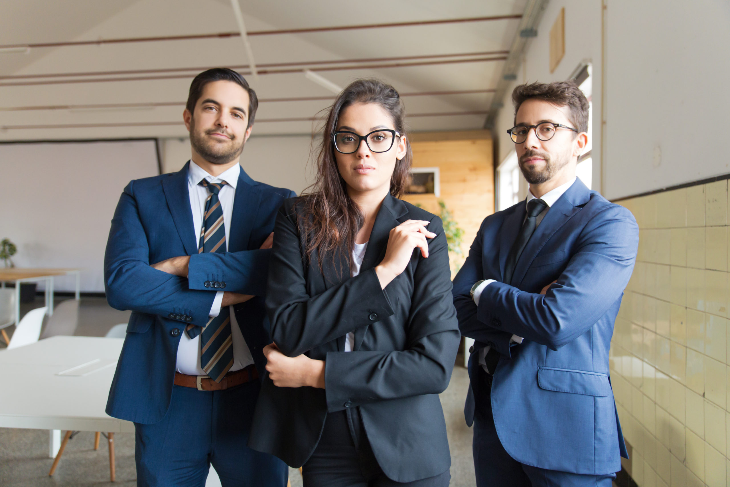 Confident young business people posing with crossed arms. Serious team of young managers standing in office. Business concept